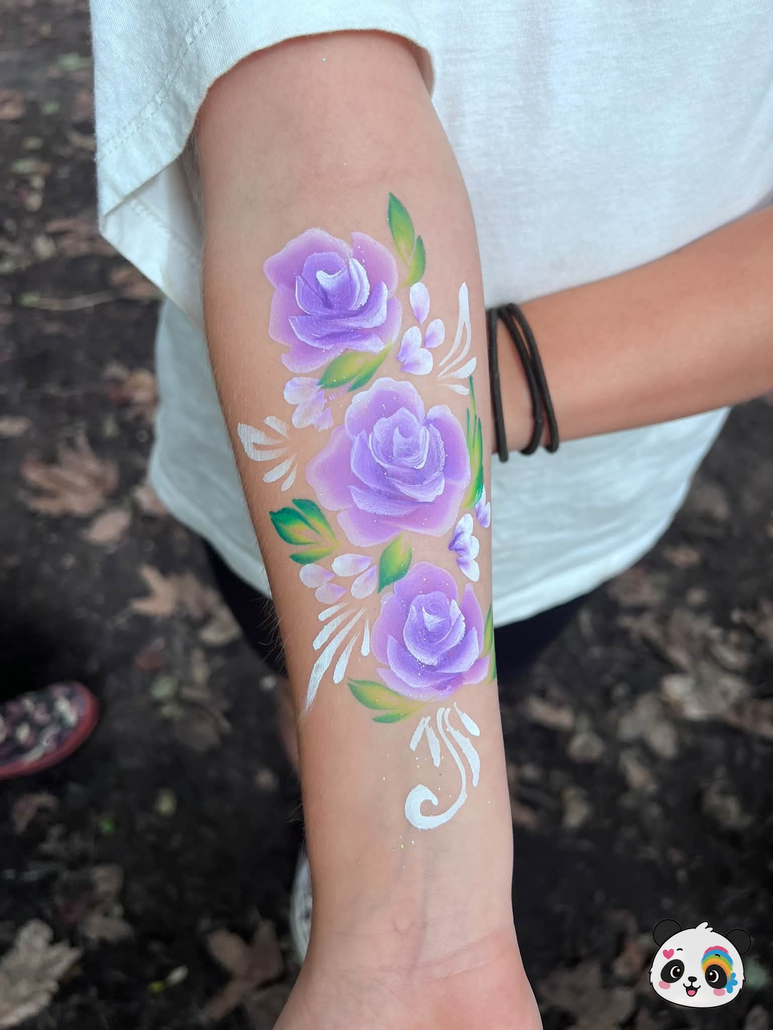 Three purple roses with green leaves and white decorative swirls painted on an arm.