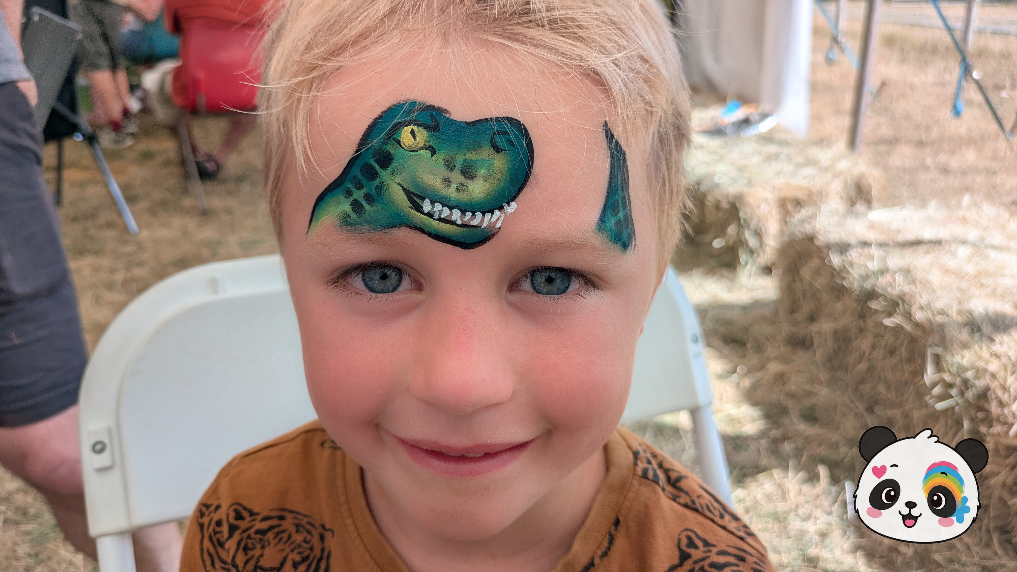 Green and black T-Rex dinosaur face paint with yellow eyes and white teeth painted on the forehead.