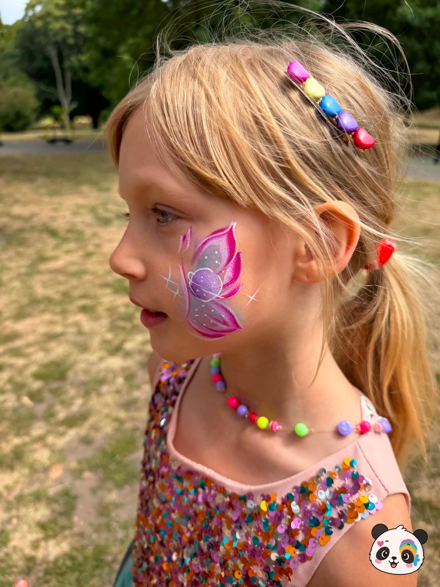 Pink and purple butterfly face paint with a planet design on the wing, accented with white stars on the cheek.