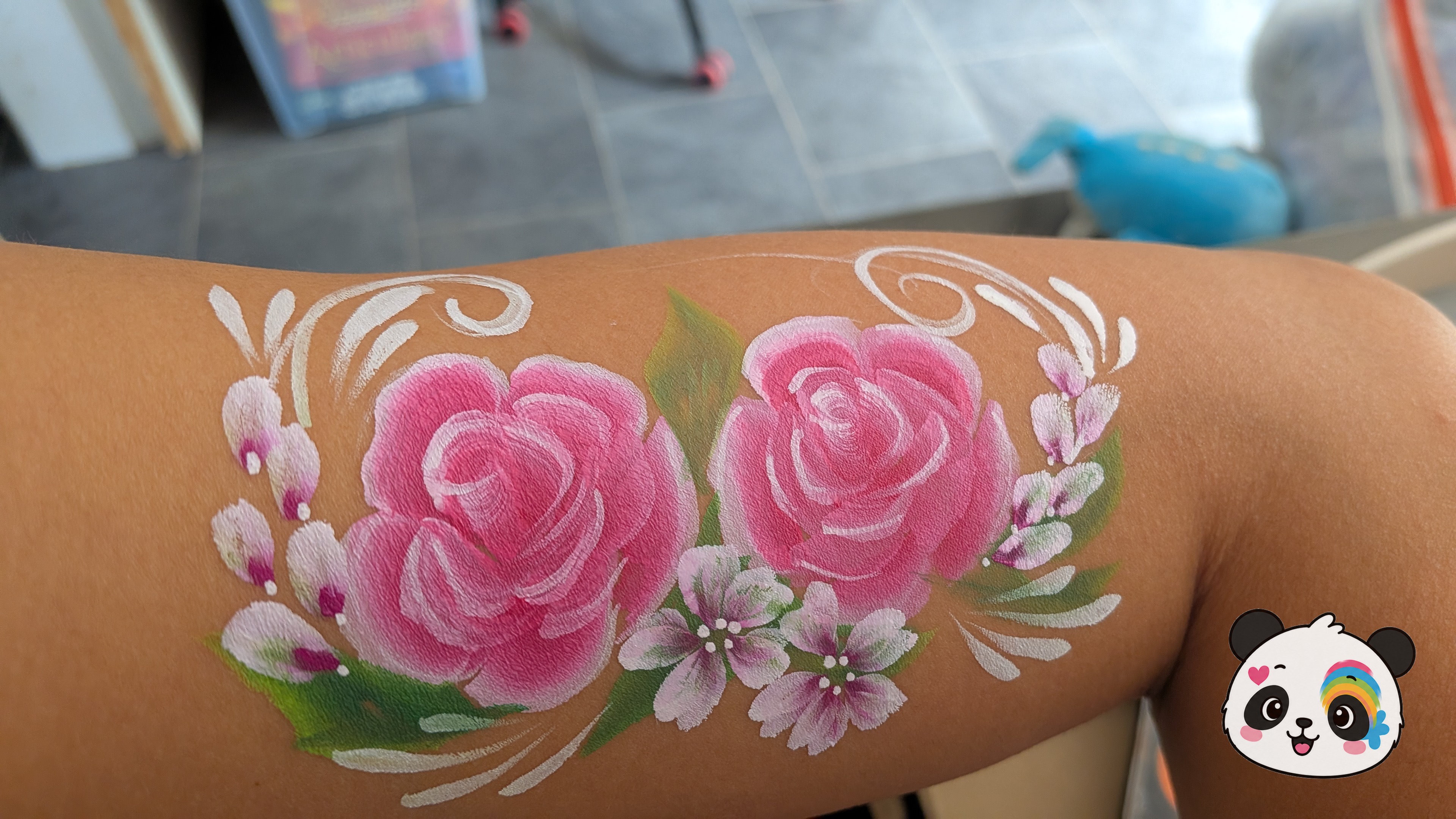 Two large pink roses surrounded by small white flowers, green leaves, and white swirls painted on an arm.
