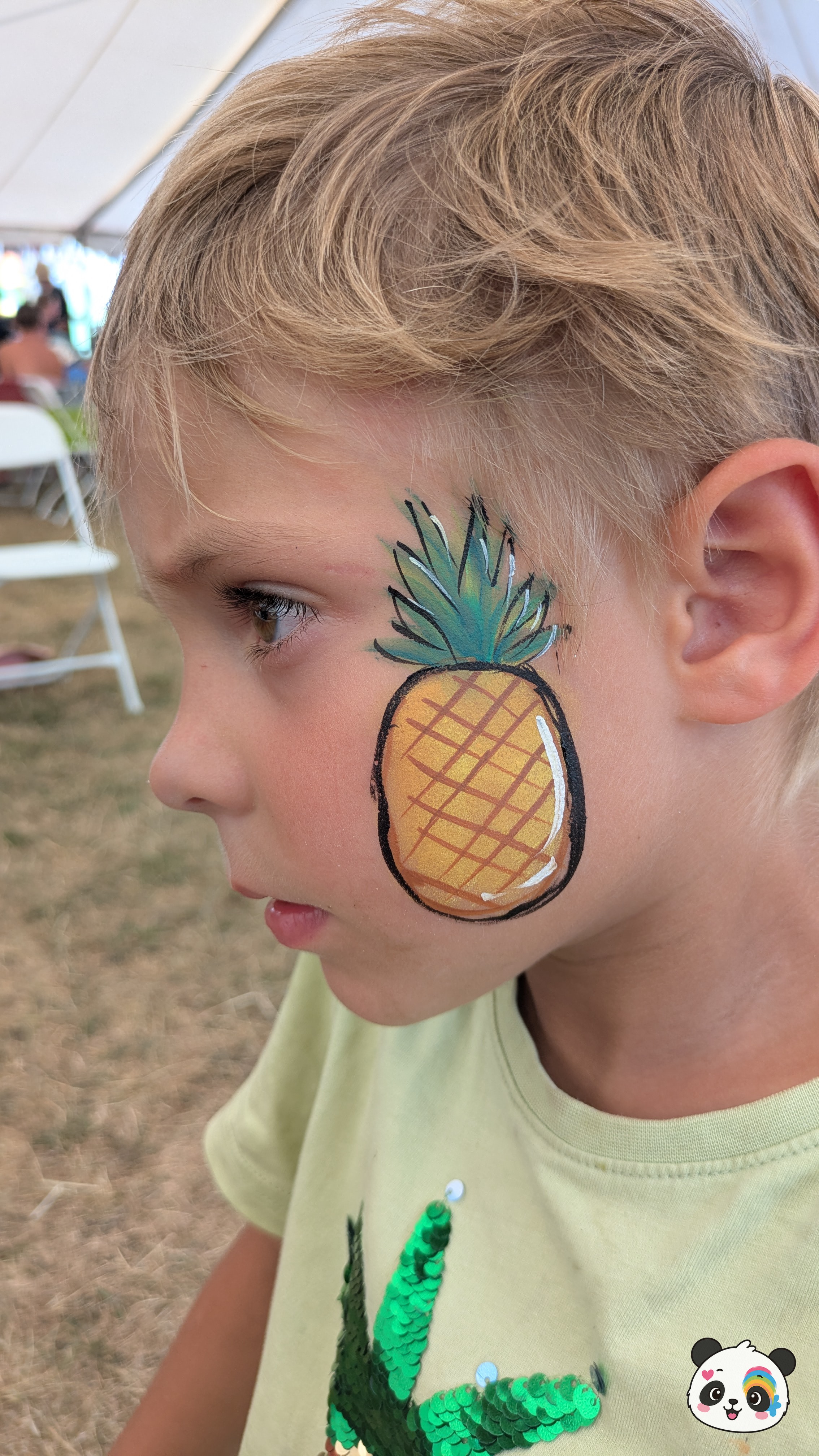 Yellow and orange pineapple face paint with green leaves on the cheek.