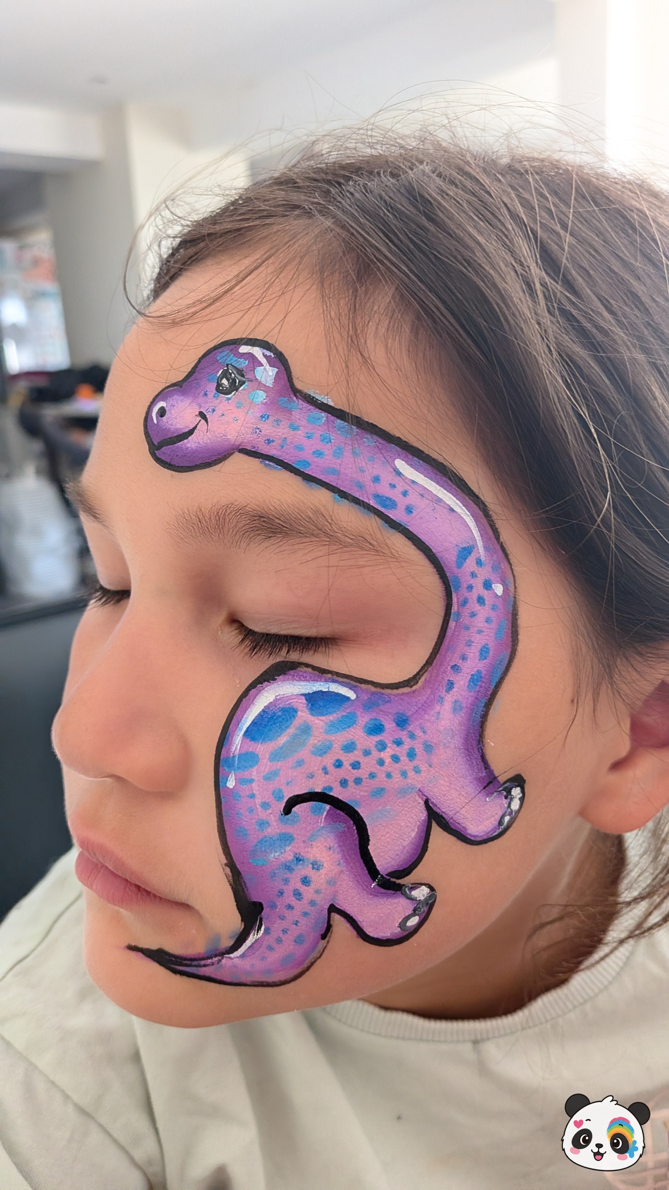 Purple and blue spotted dinosaur face paint design extending from the forehead down to the cheek.