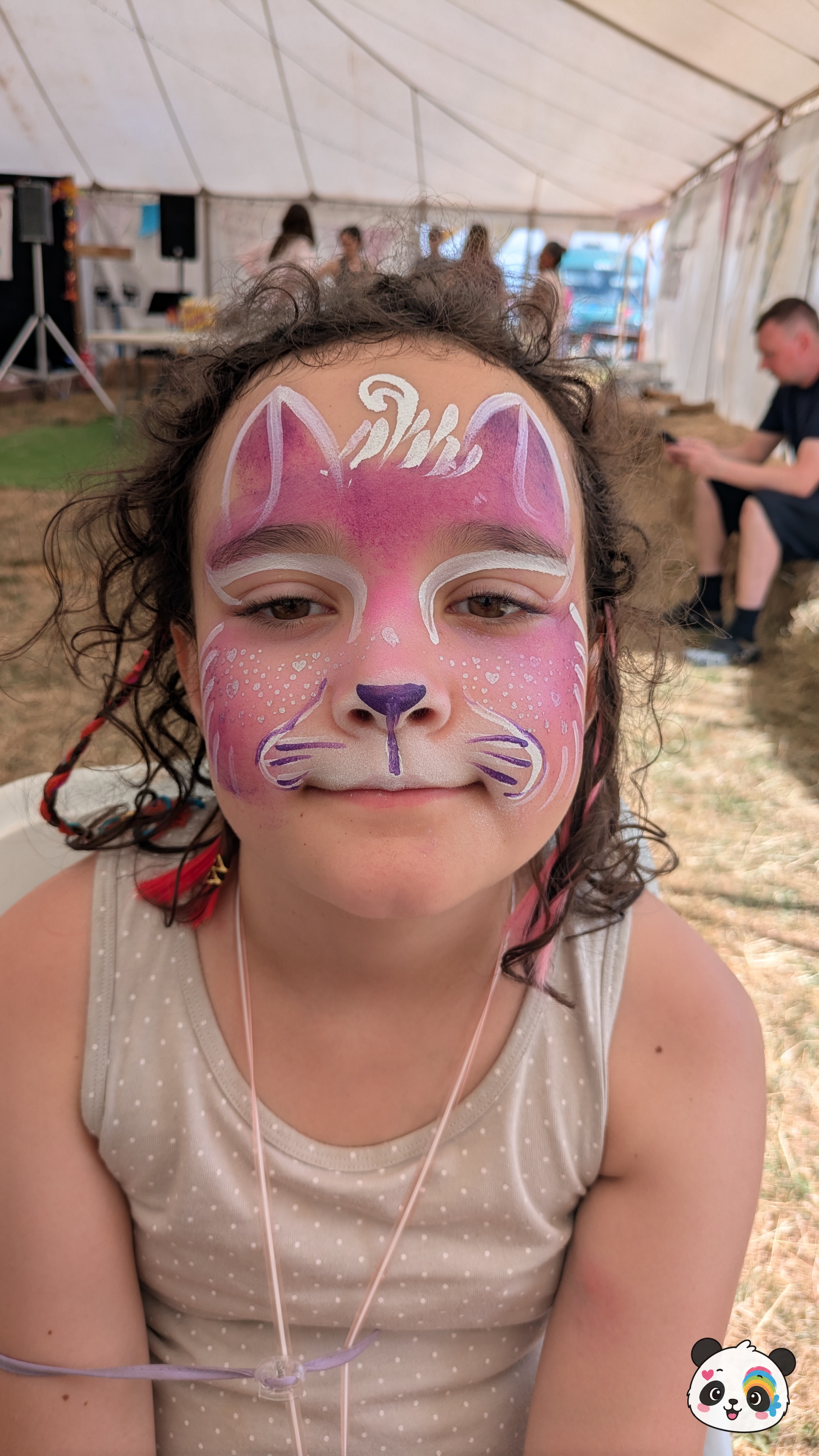 Pink and white cat face paint featuring purple nose details, whiskers, and decorative white swirls on the forehead.