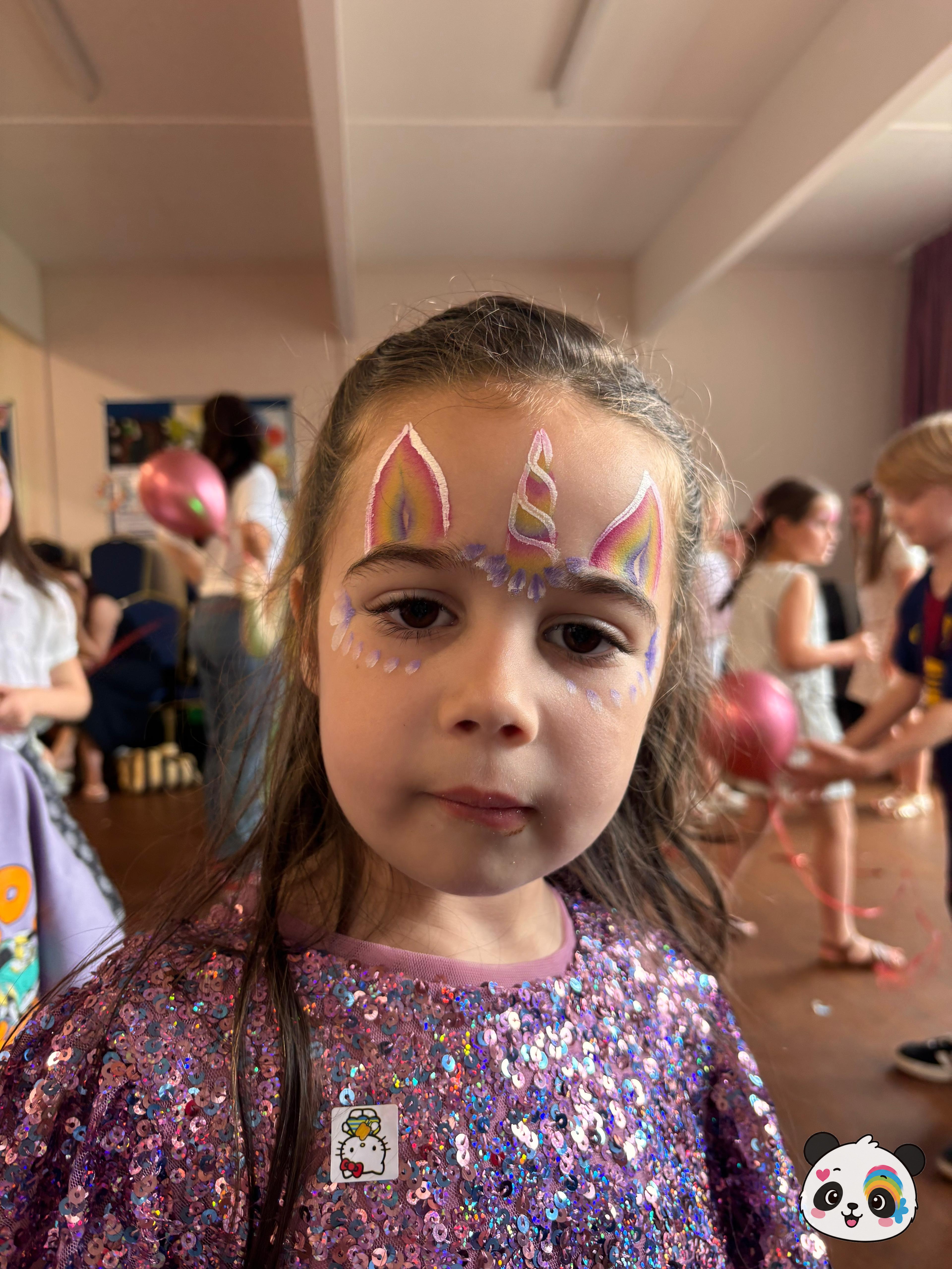 Rainbow unicorn horn and ears painted on the forehead with purple accents extending to the temples.