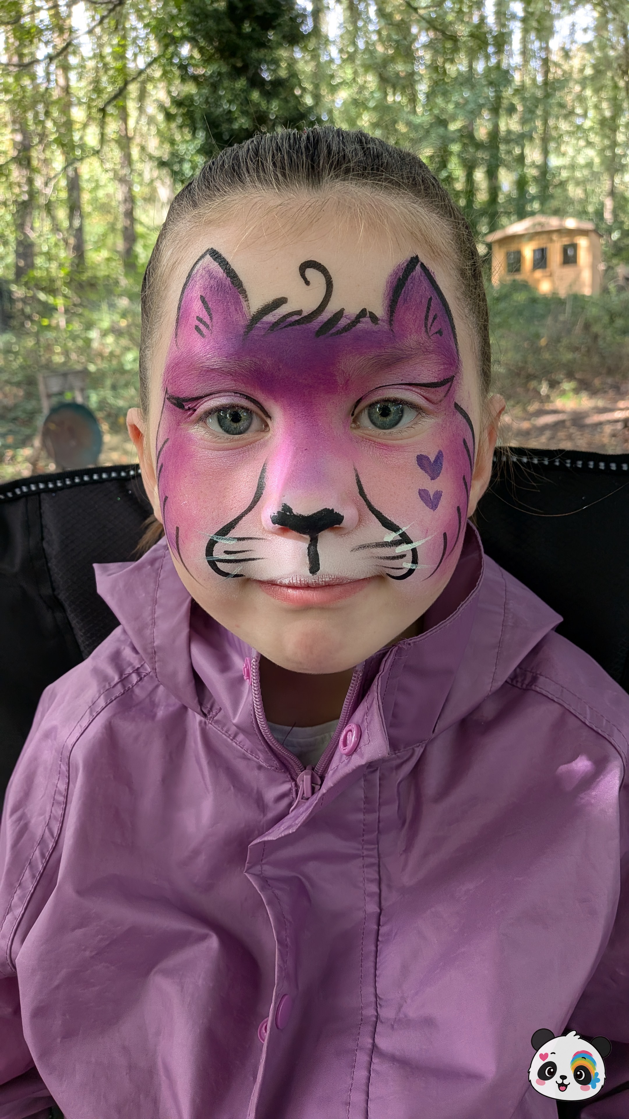 Purple and pink cat face paint covering the forehead and cheeks, featuring black outlines, whiskers, and small heart accents.