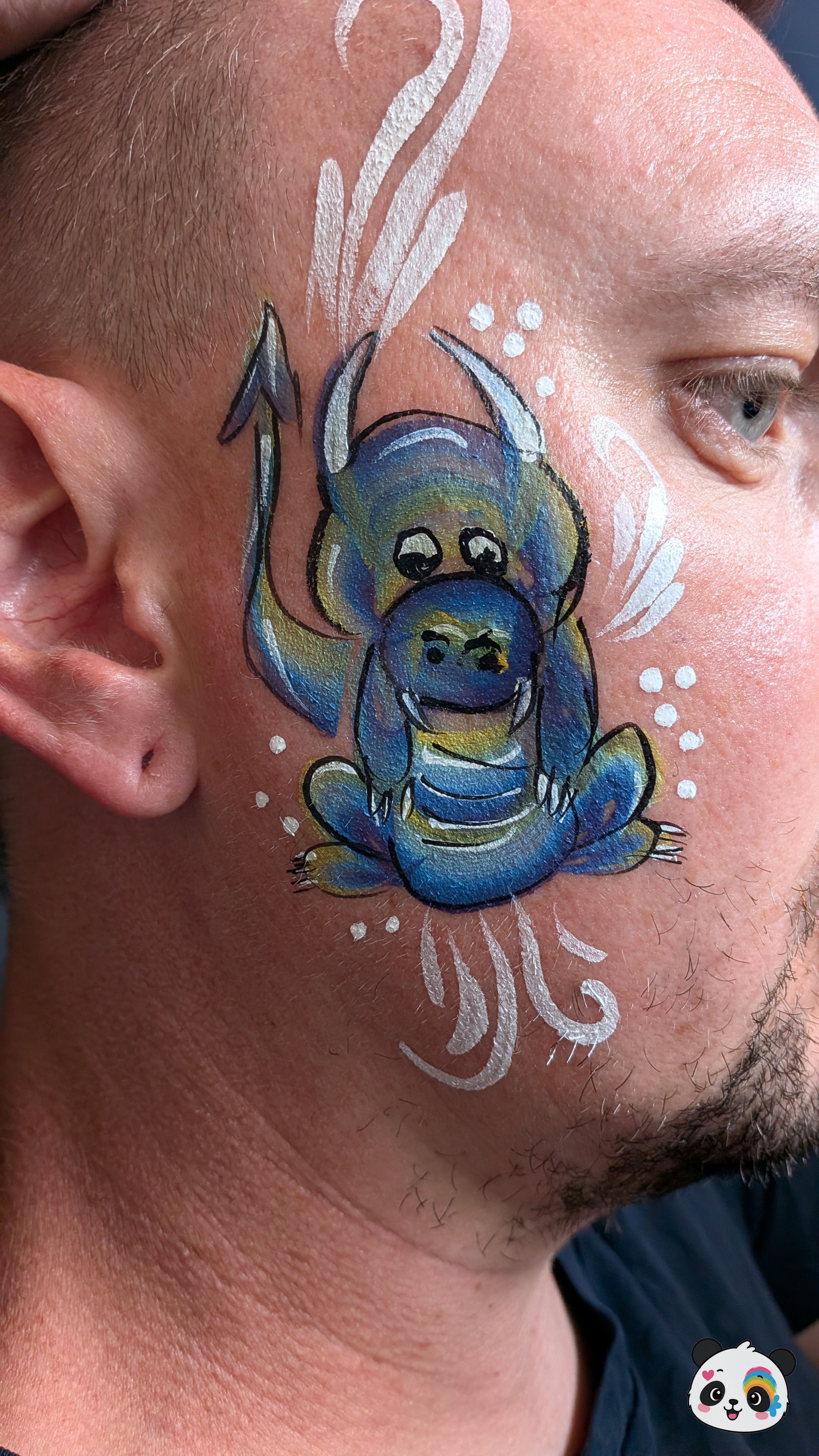 Blue and yellow dragon face paint with white decorative swirls on the cheek.