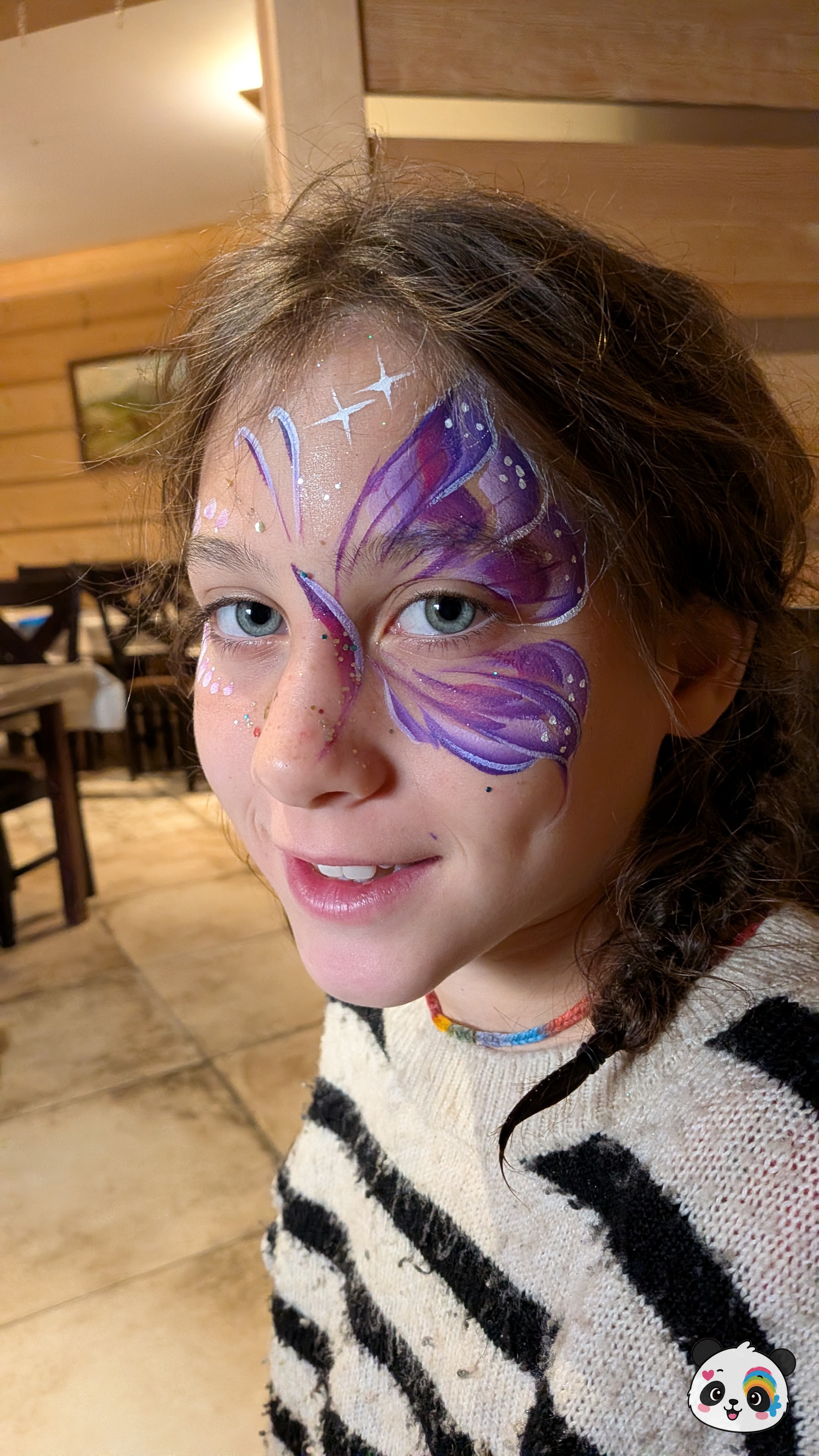 Purple and white butterfly wing face paint design covering one eye and extending to the forehead, accented with white star details and glitter.
