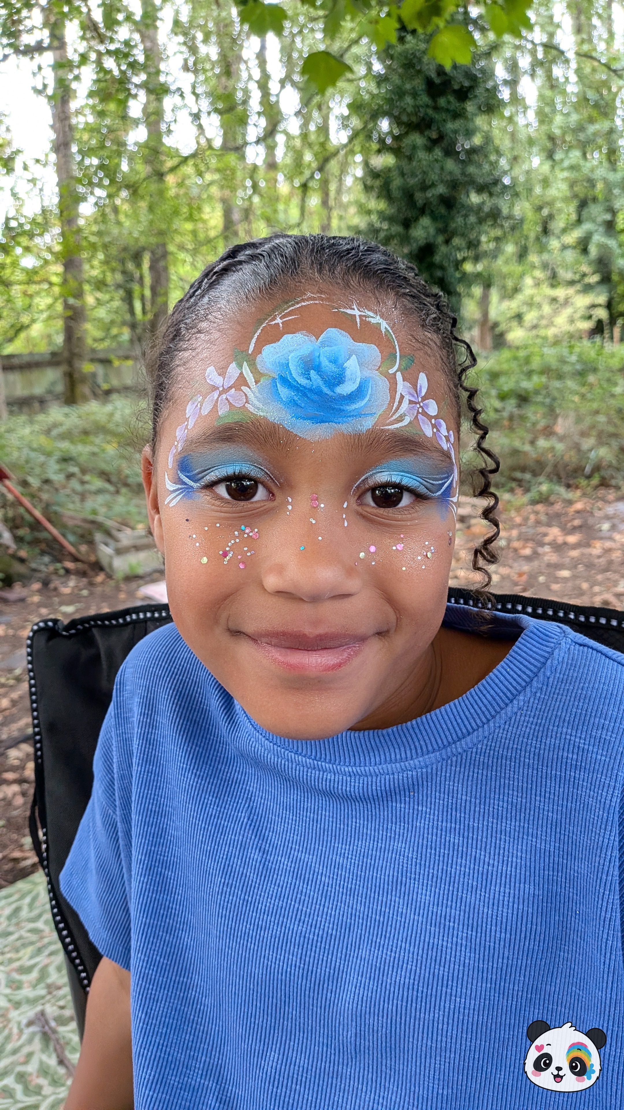 Blue rose forehead design with white flowers, blue eyeshadow, and glitter accents on the cheeks.