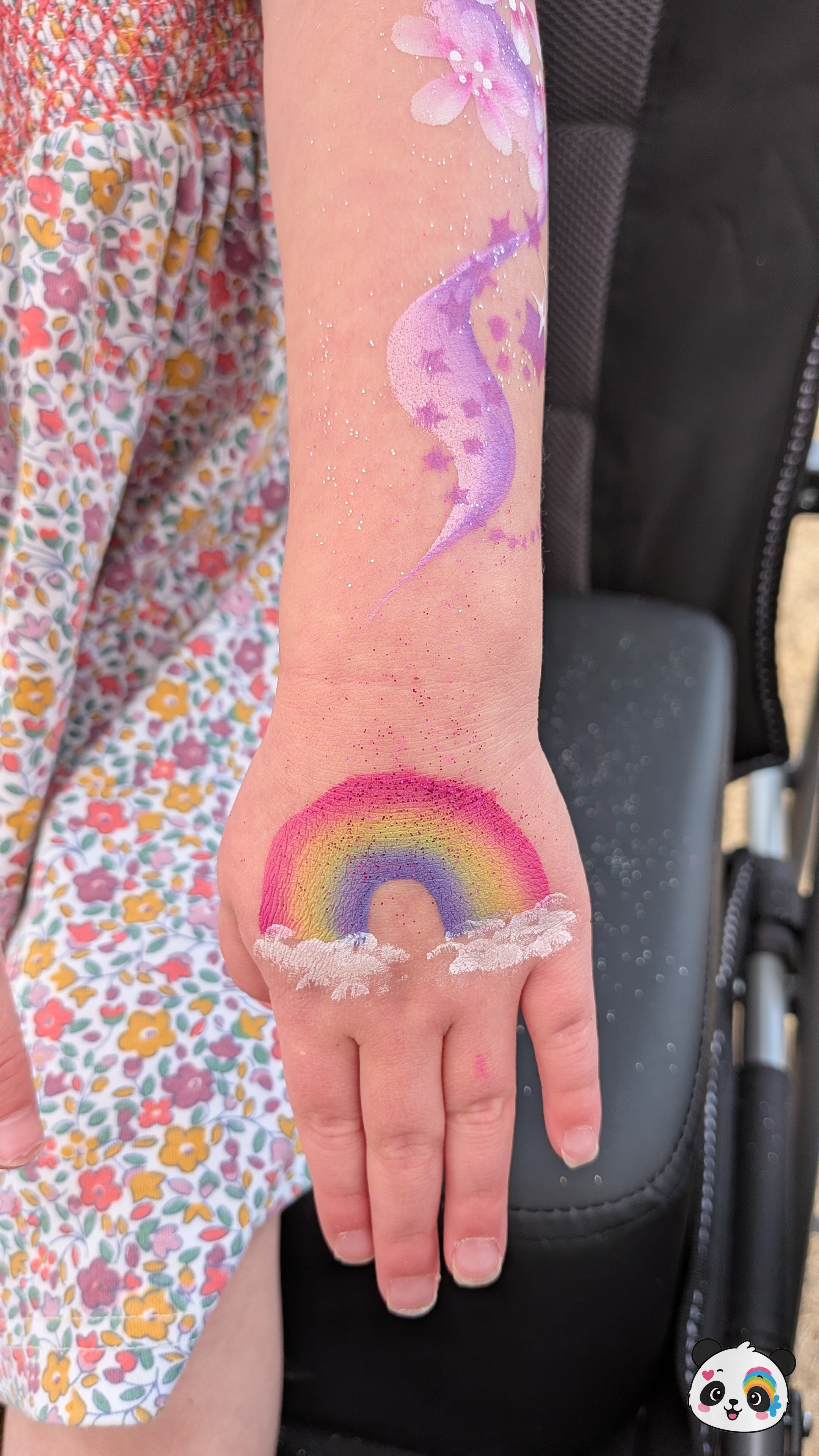 A colorful rainbow with white clouds on the hand and a purple star-themed design with flowers on the forearm.