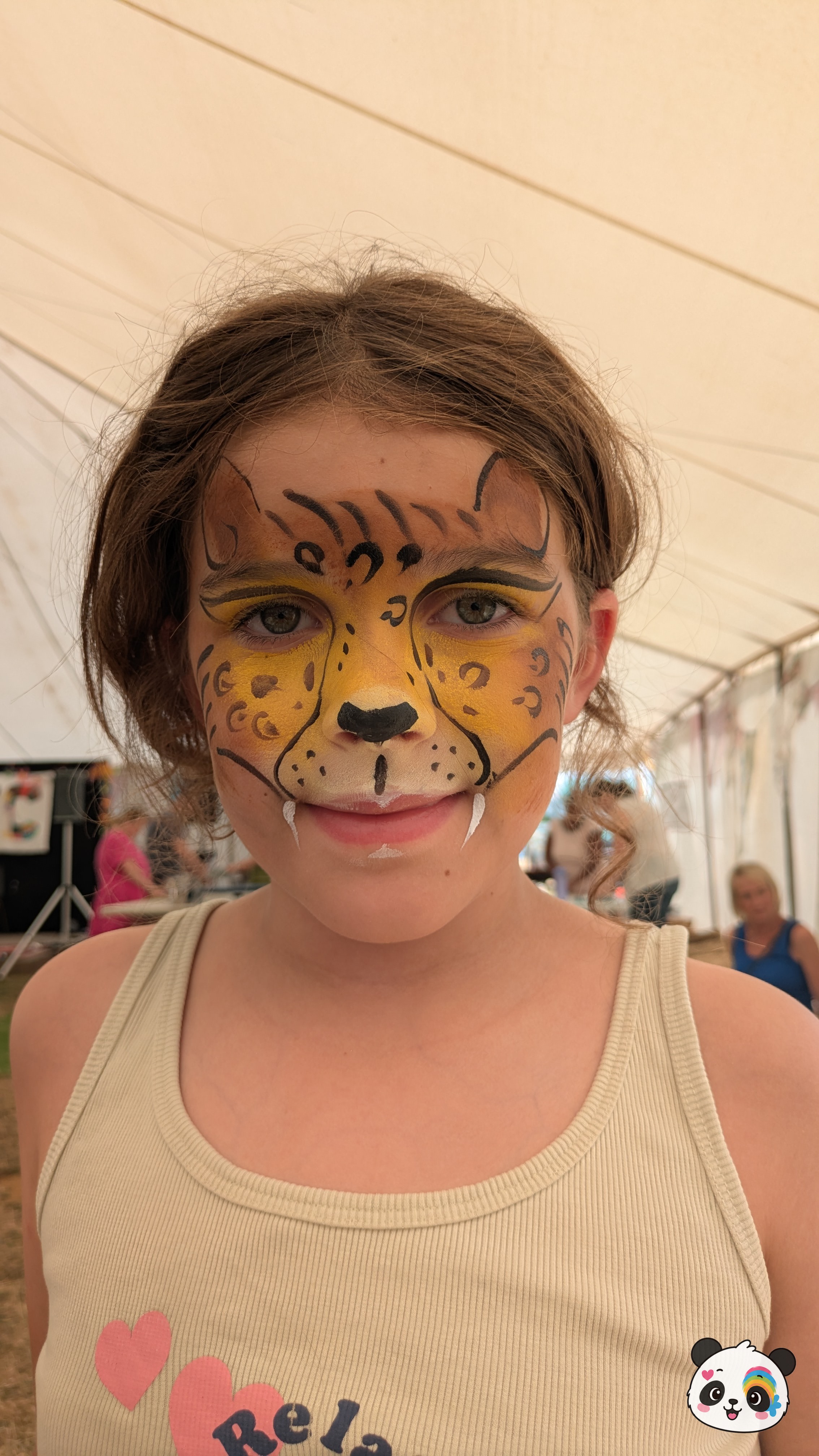 Yellow and orange cheetah face paint with black spots, a black nose, and white fangs on the upper lip.
