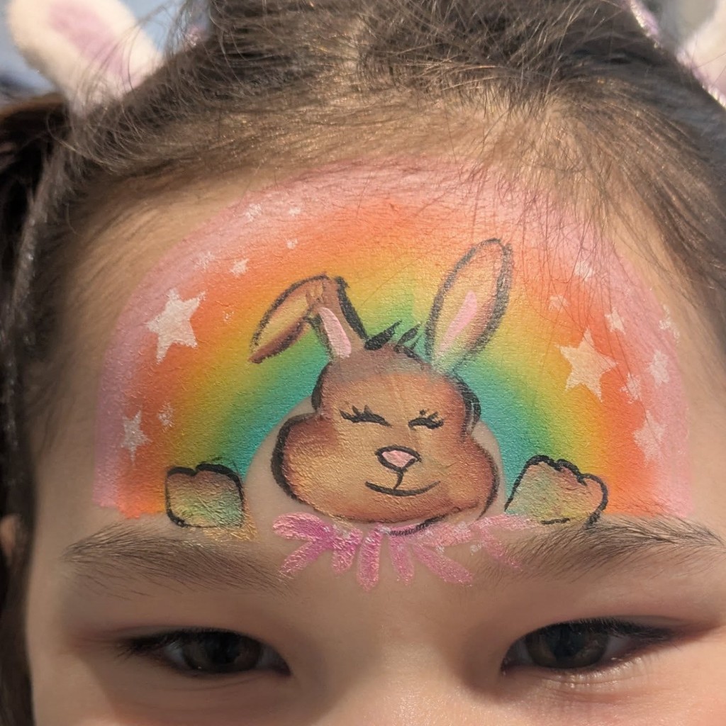 Cute bunny face paint on a rainbow background across a child's forehead