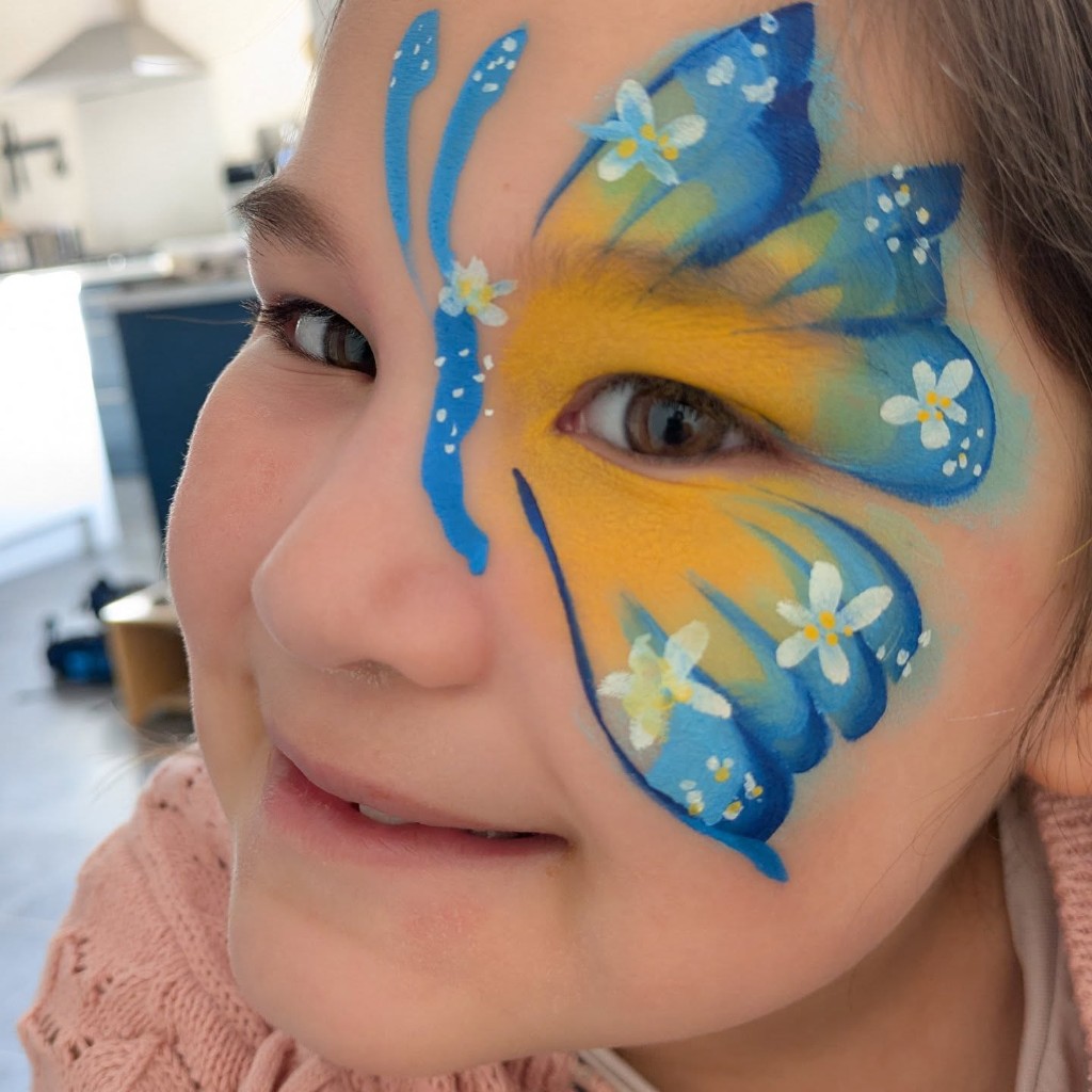 Blue and yellow butterfly wing face paint with white flowers