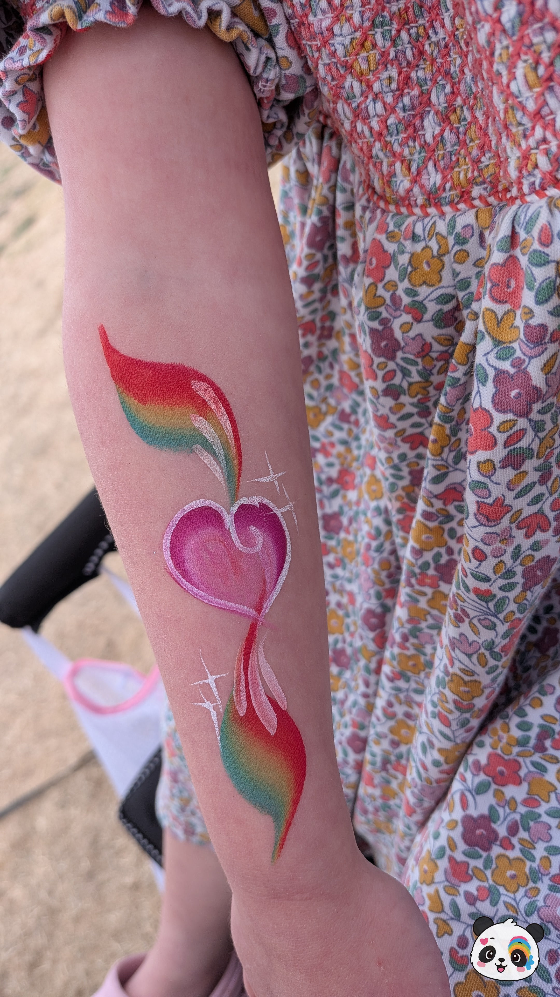 A pink heart with rainbow-colored flame accents and white star details painted on an arm.