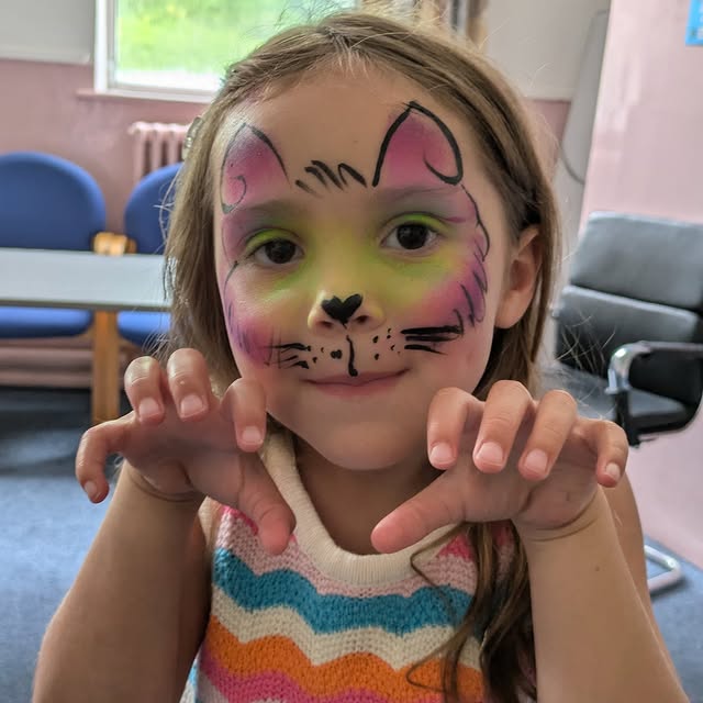 Pink and green cat face paint with whiskers on a smiling child