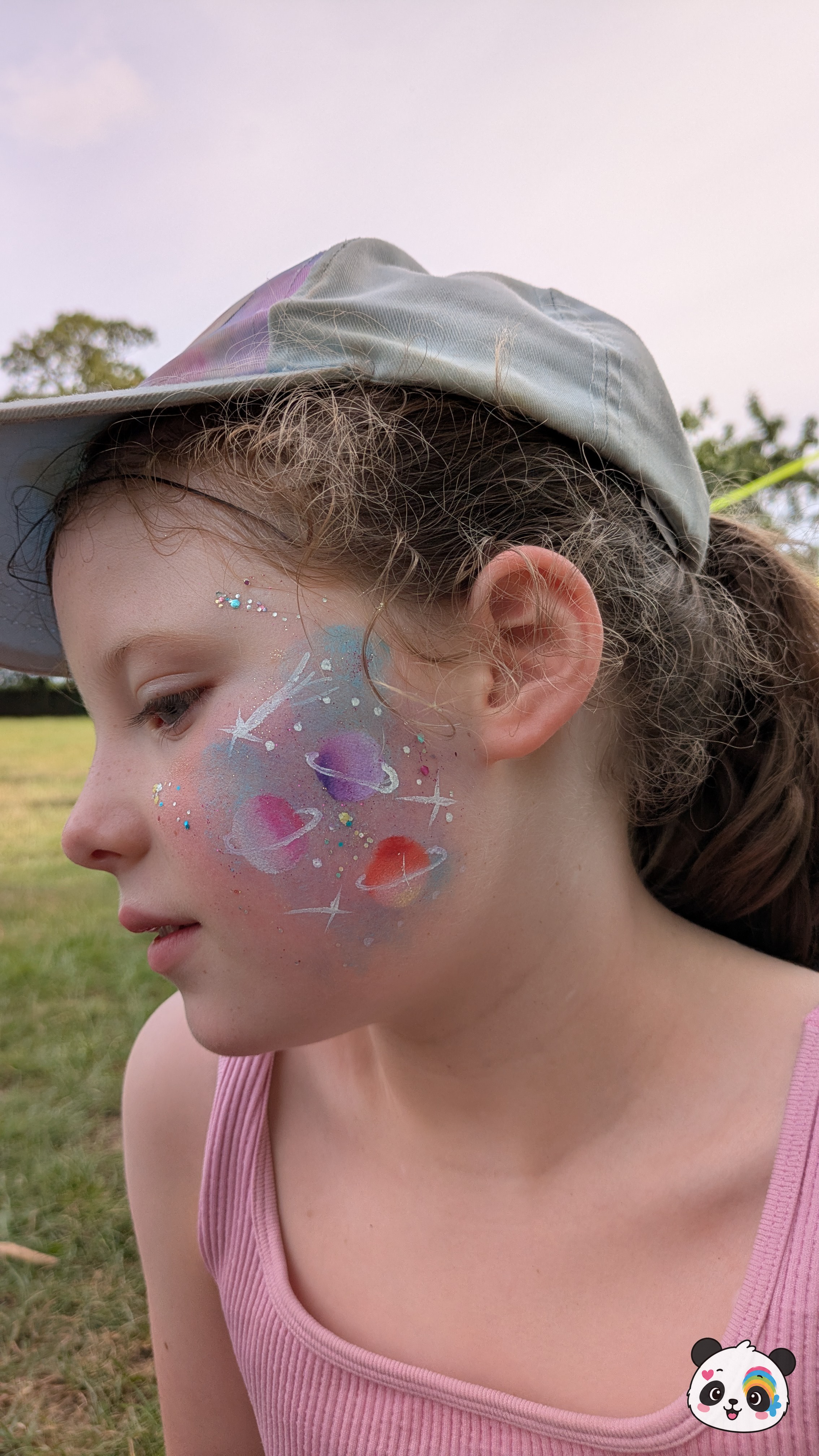 Colorful galaxy and planet face paint with white stars and glitter accents on the cheek.
