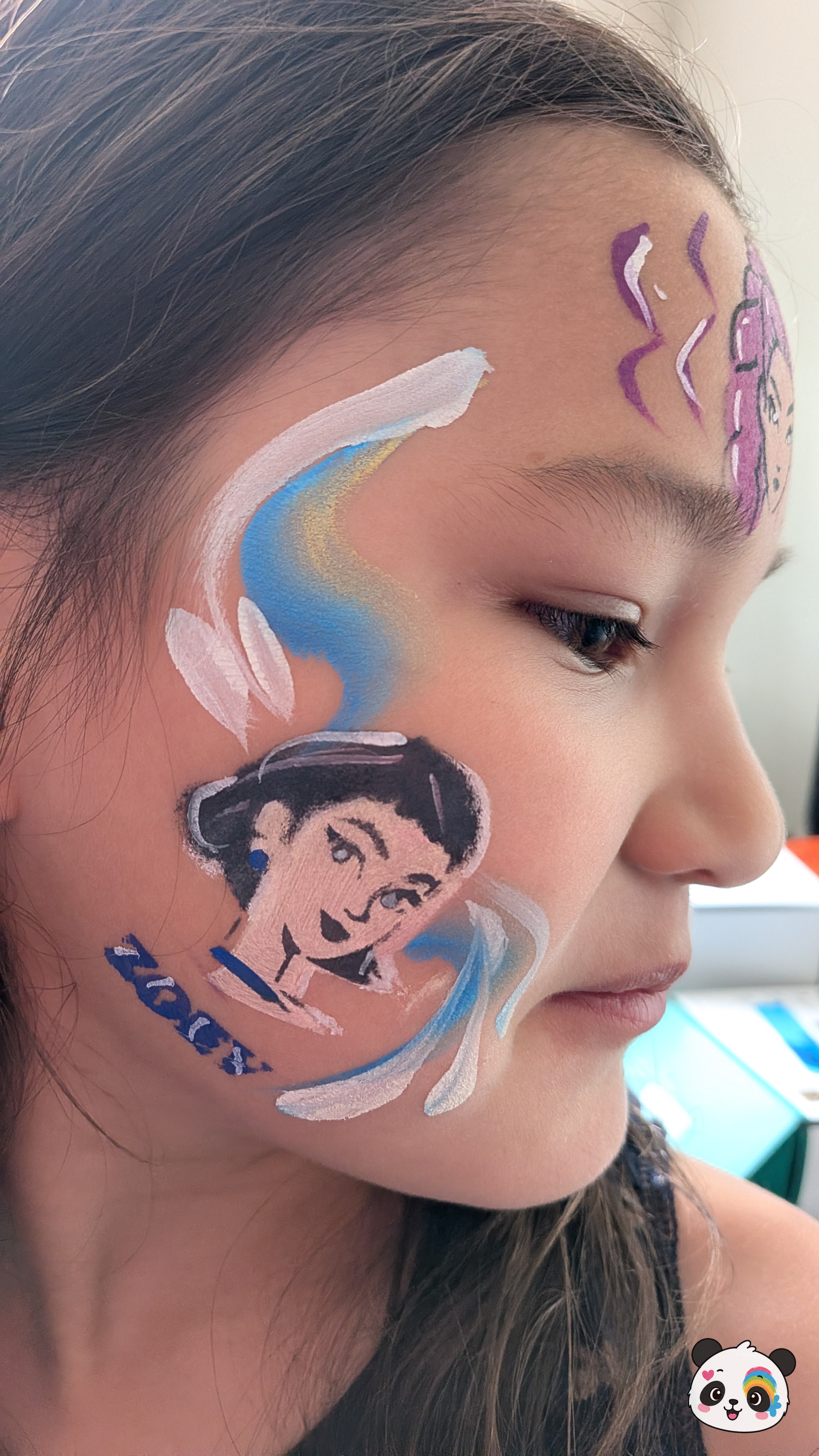 Princess Jasmine character face paint on the cheek with blue and white swirling accents and purple forehead details.
