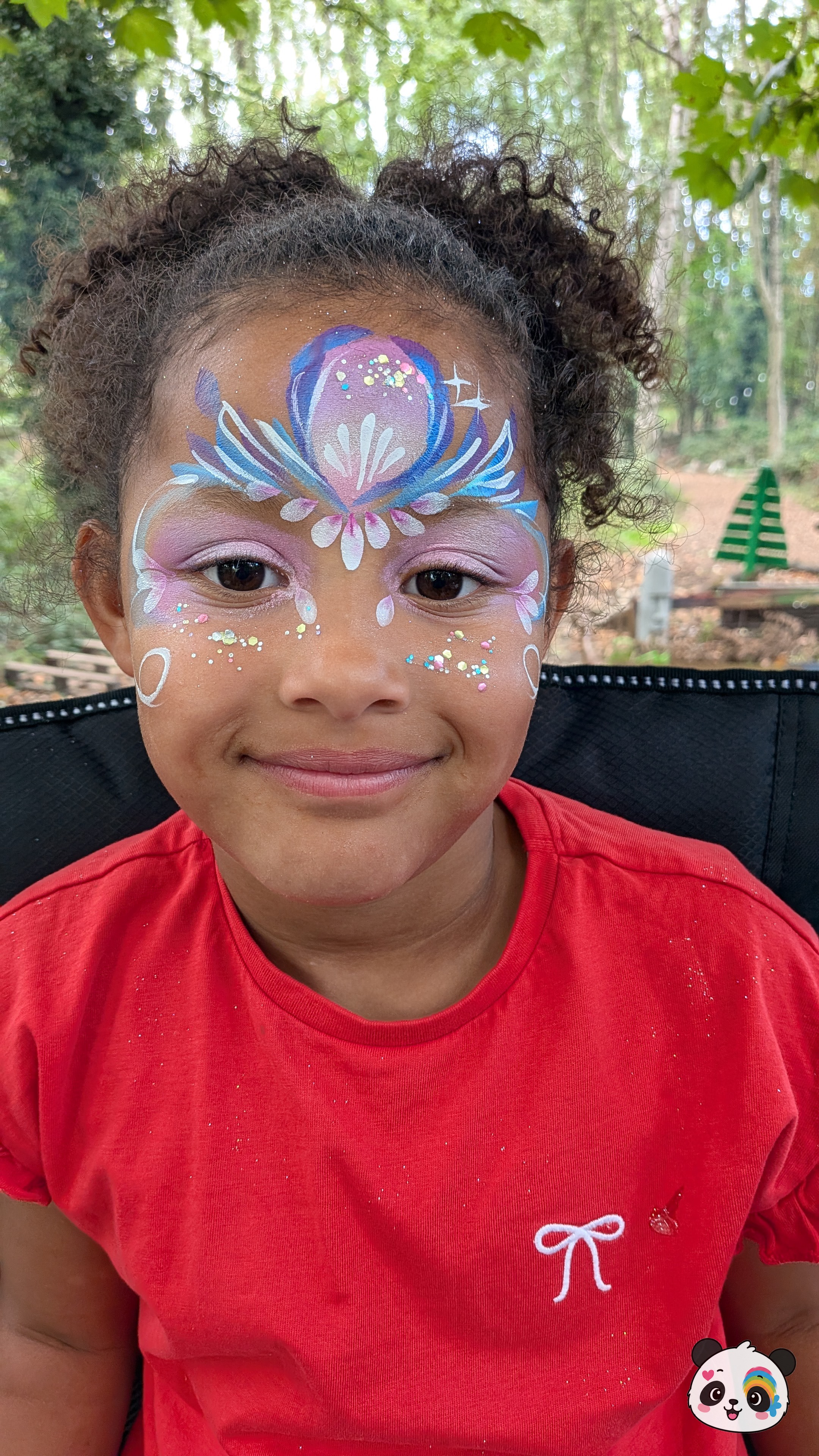 Purple, blue, and white floral fairy mask face paint with glitter accents across the forehead and eyelids.