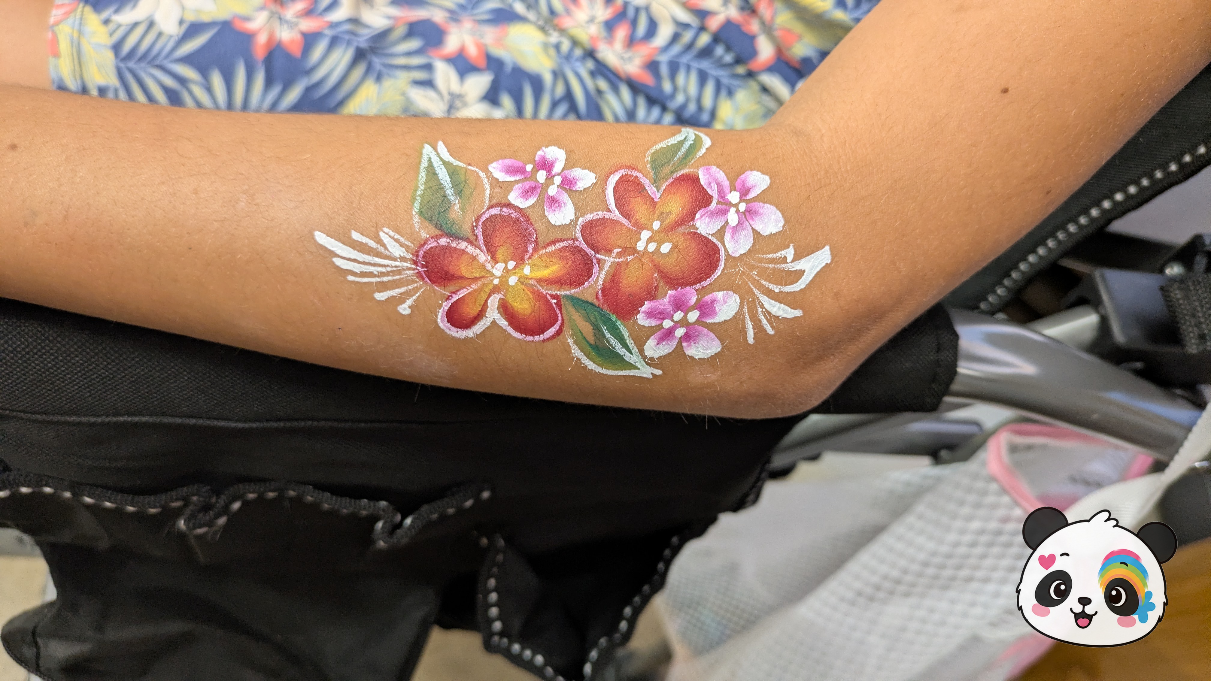 Red and orange tropical flowers with pink accents, green leaves, and white decorative swirls painted on an arm.