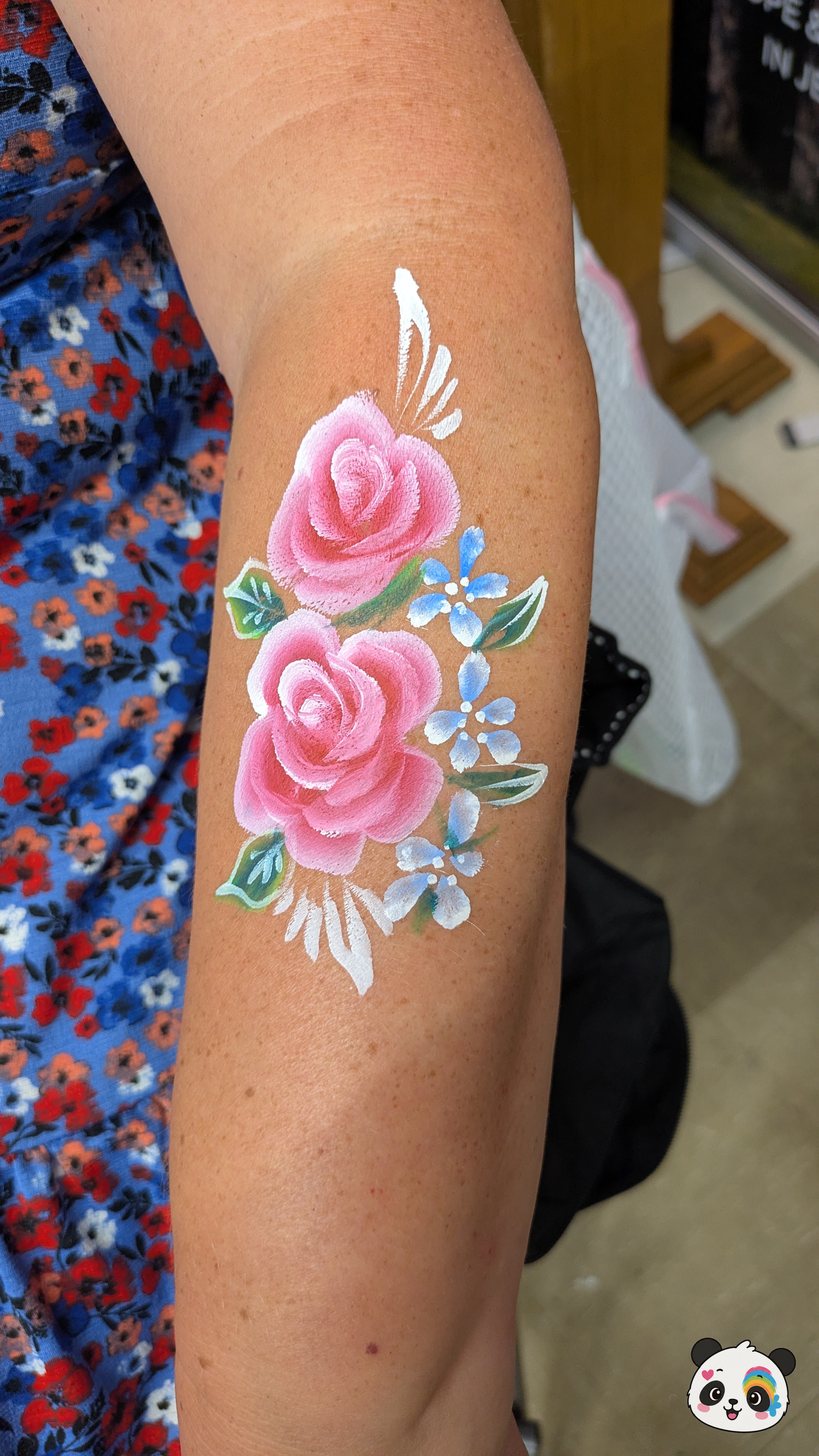 Pink roses with blue accent flowers and green leaves painted on an arm.