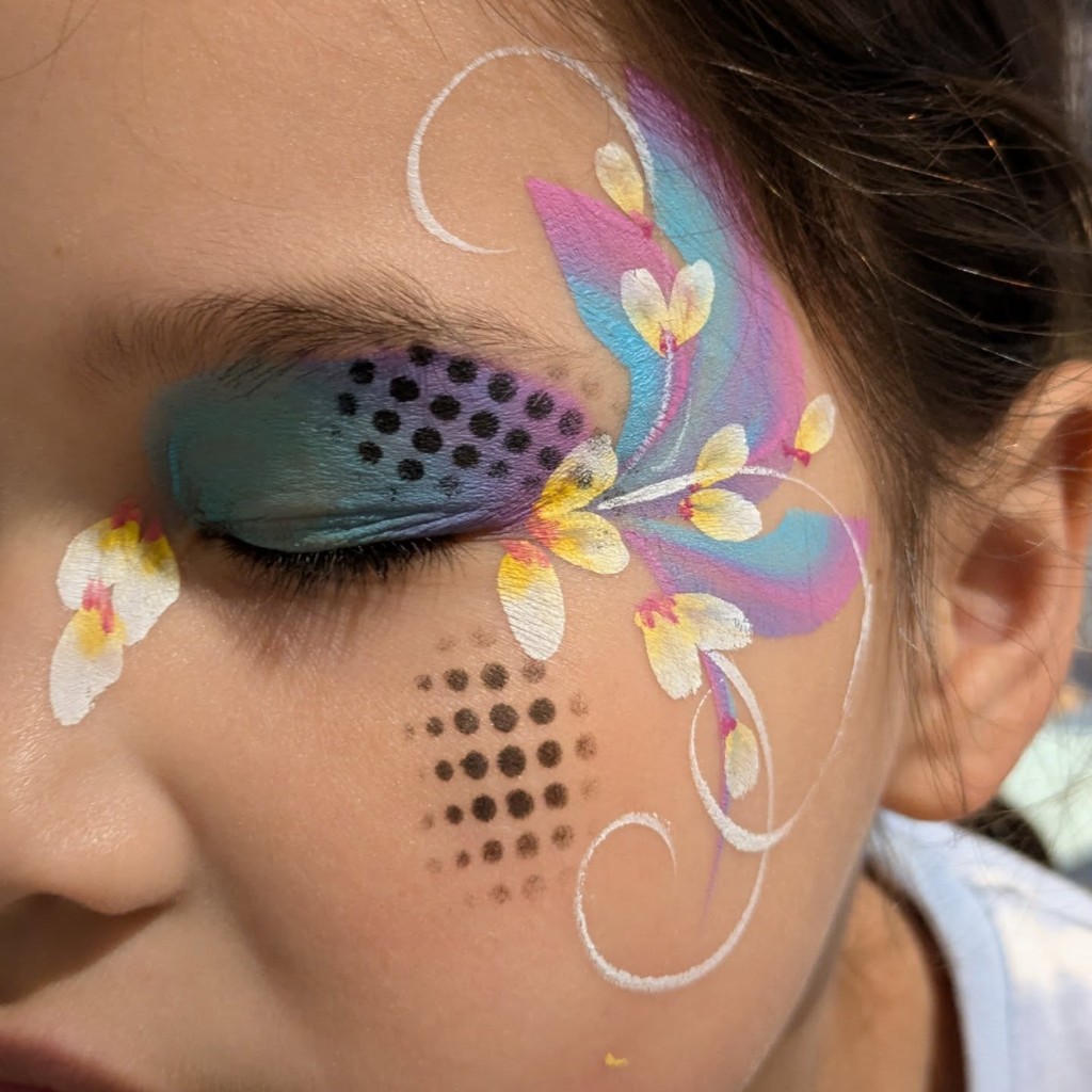 Teal and purple floral face paint with white blossoms around the eye