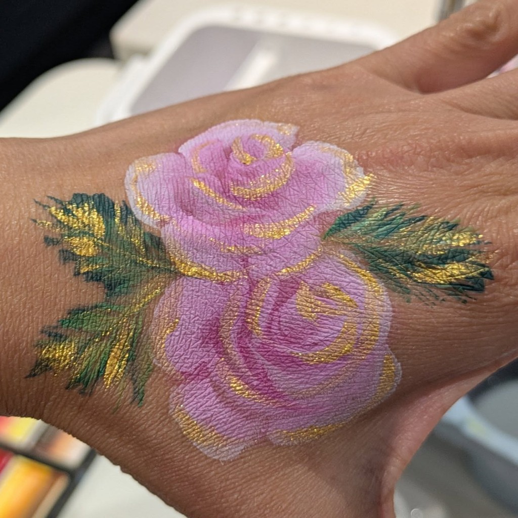 Pink roses with gold highlights painted on the back of a hand