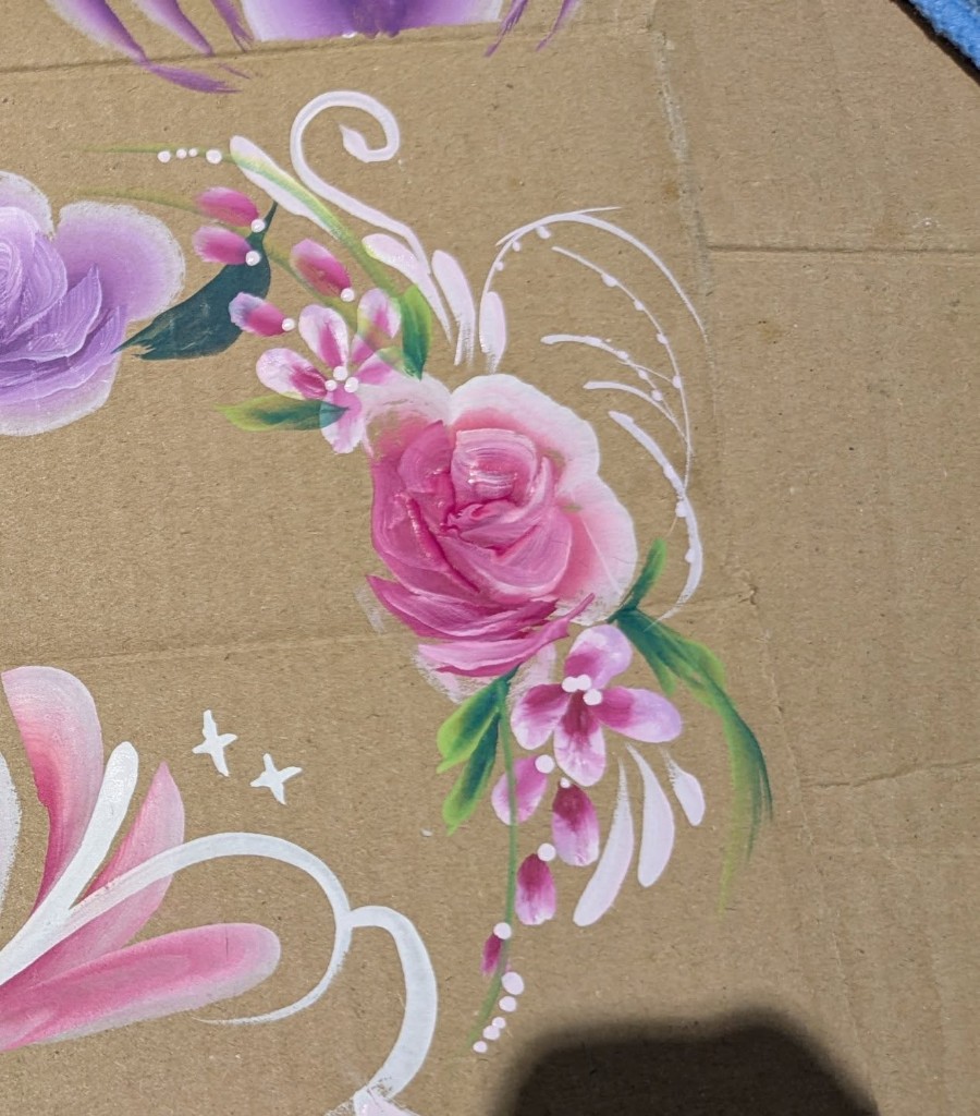 Pink rose and floral designs painted on a brown practice board